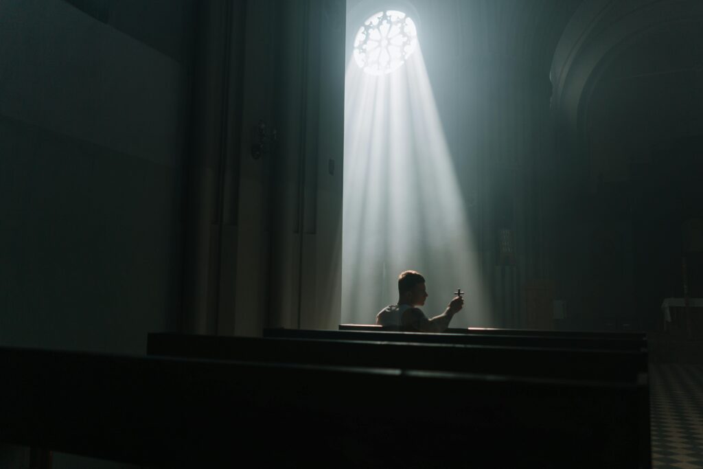 A person sits praying inside a church, illuminated by rays of sunlight through a window.